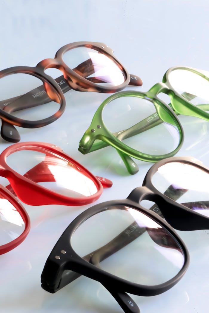 A collection of various colored eyeglasses displayed on a reflective surface, highlighting modern fashion.